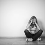 girl sits in depression on floor near the wall